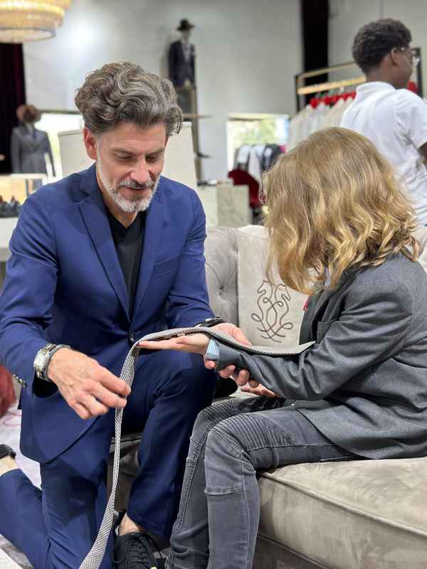 A volunteer tying a bow tie for a seated boy at the workshop
