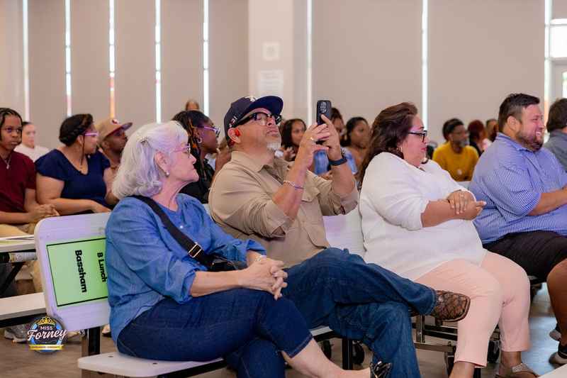 Seated audience at the Miss Forney Scholarship Pageant, one man photographing the stage with his phone